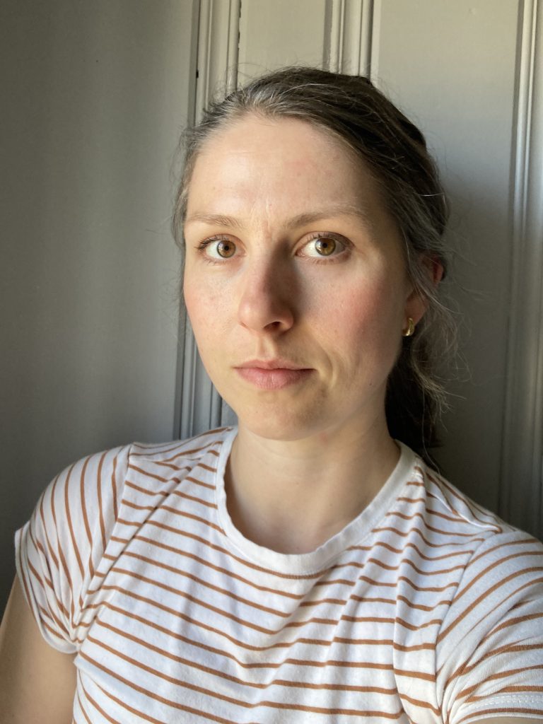 photo of the author: a white woman with brown hair in a ponytail, wearing a white-and-brown striped shirt
